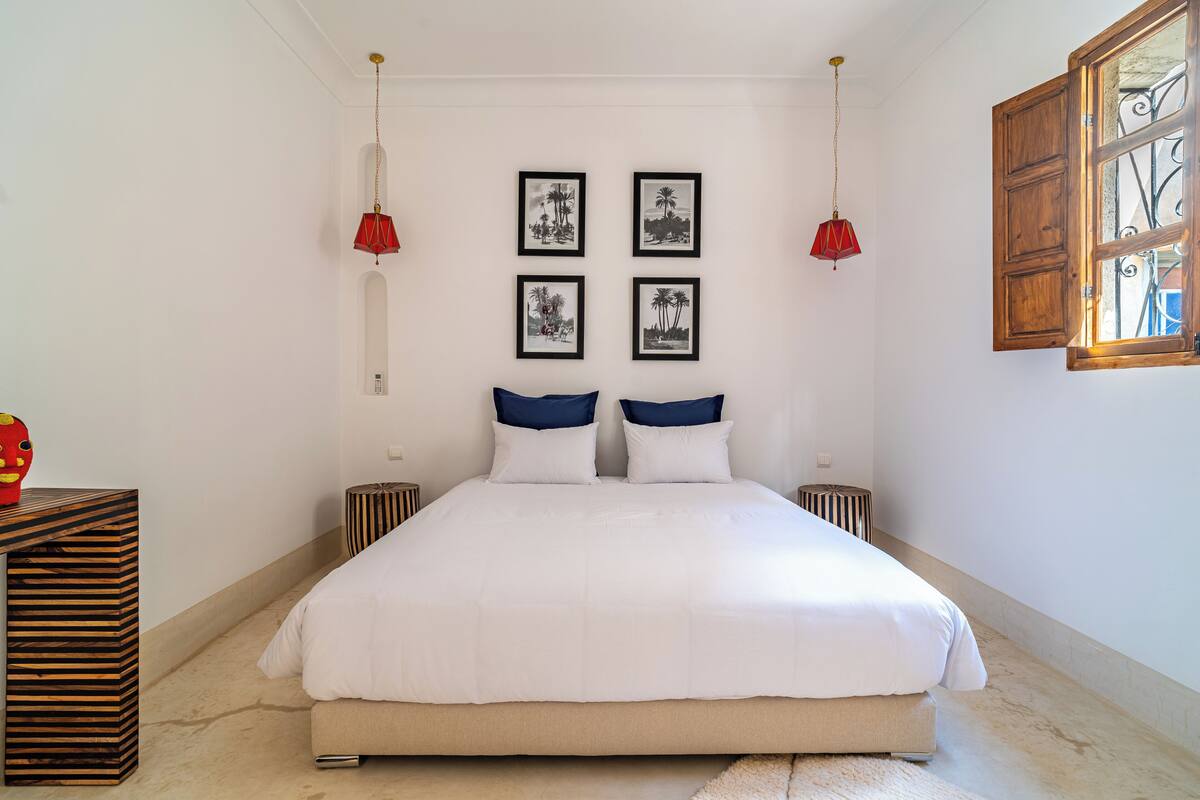 A bedroom with a large bed, two bedside tables, a wooden cabinet, and four framed pictures on the wall.