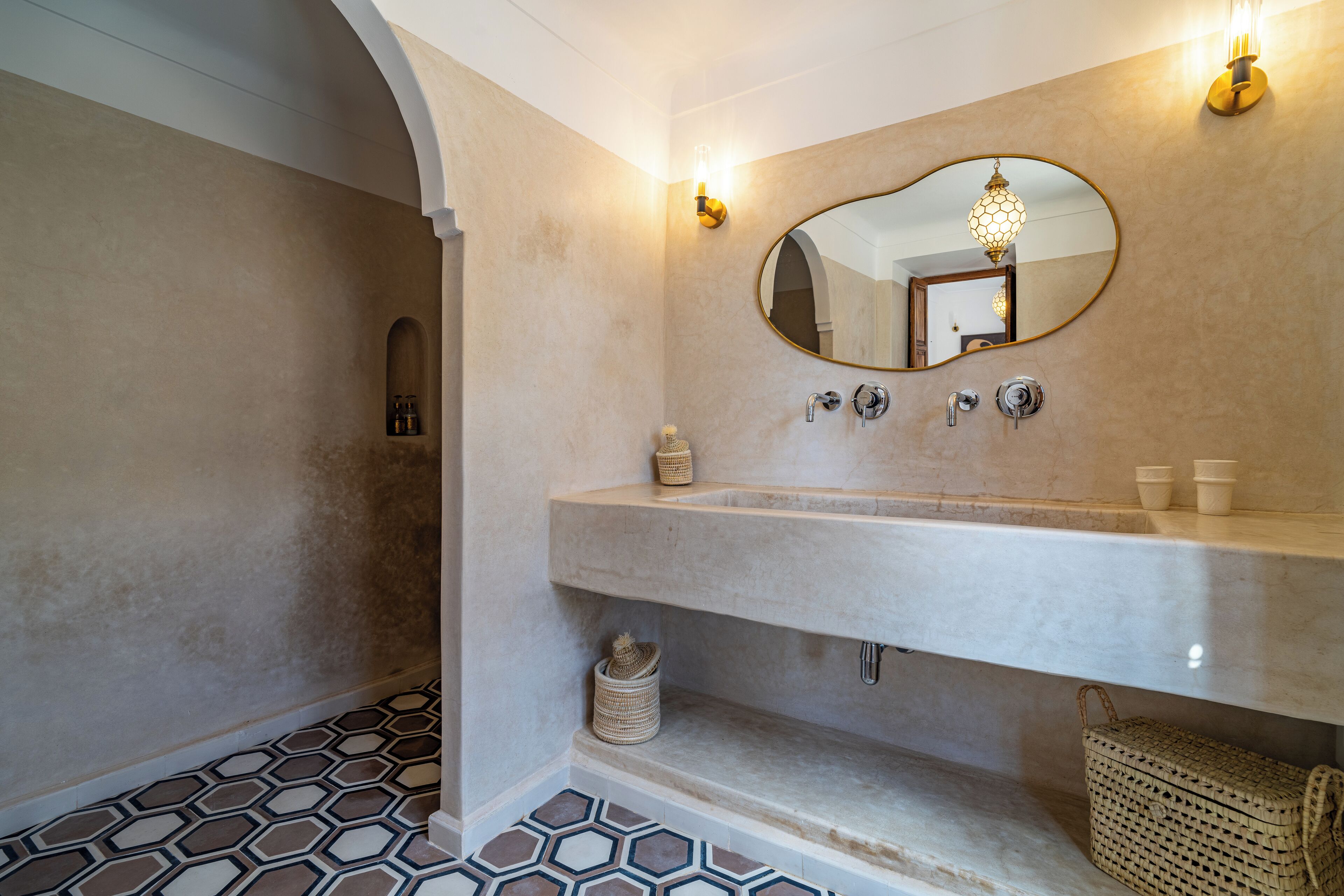 Une salle de bain dotée d’un grand miroir ovale, d’un lavabo en marbre et d’un sol à motifs hexagonaux.