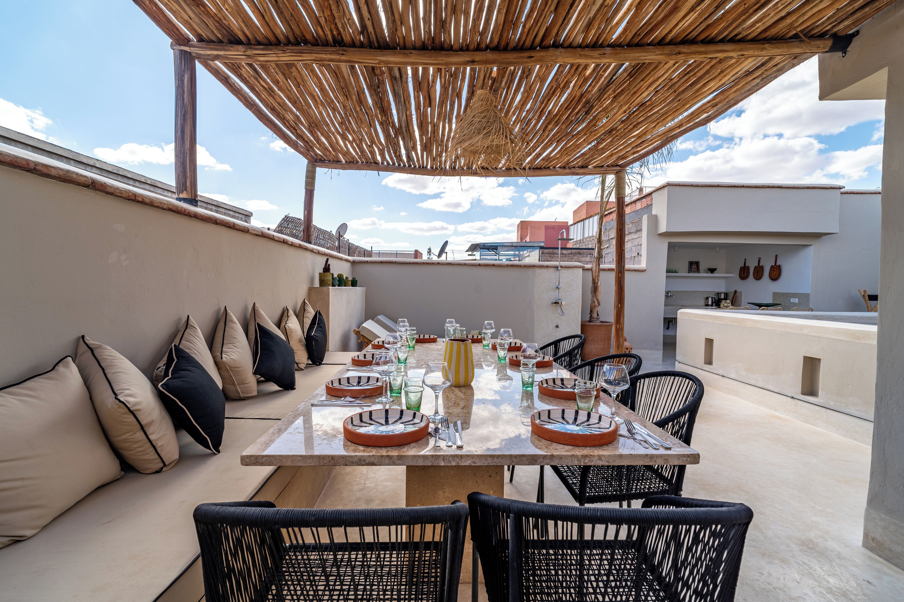 A rooftop terrace with a dining table set for six, surrounded by black wicker chairs.