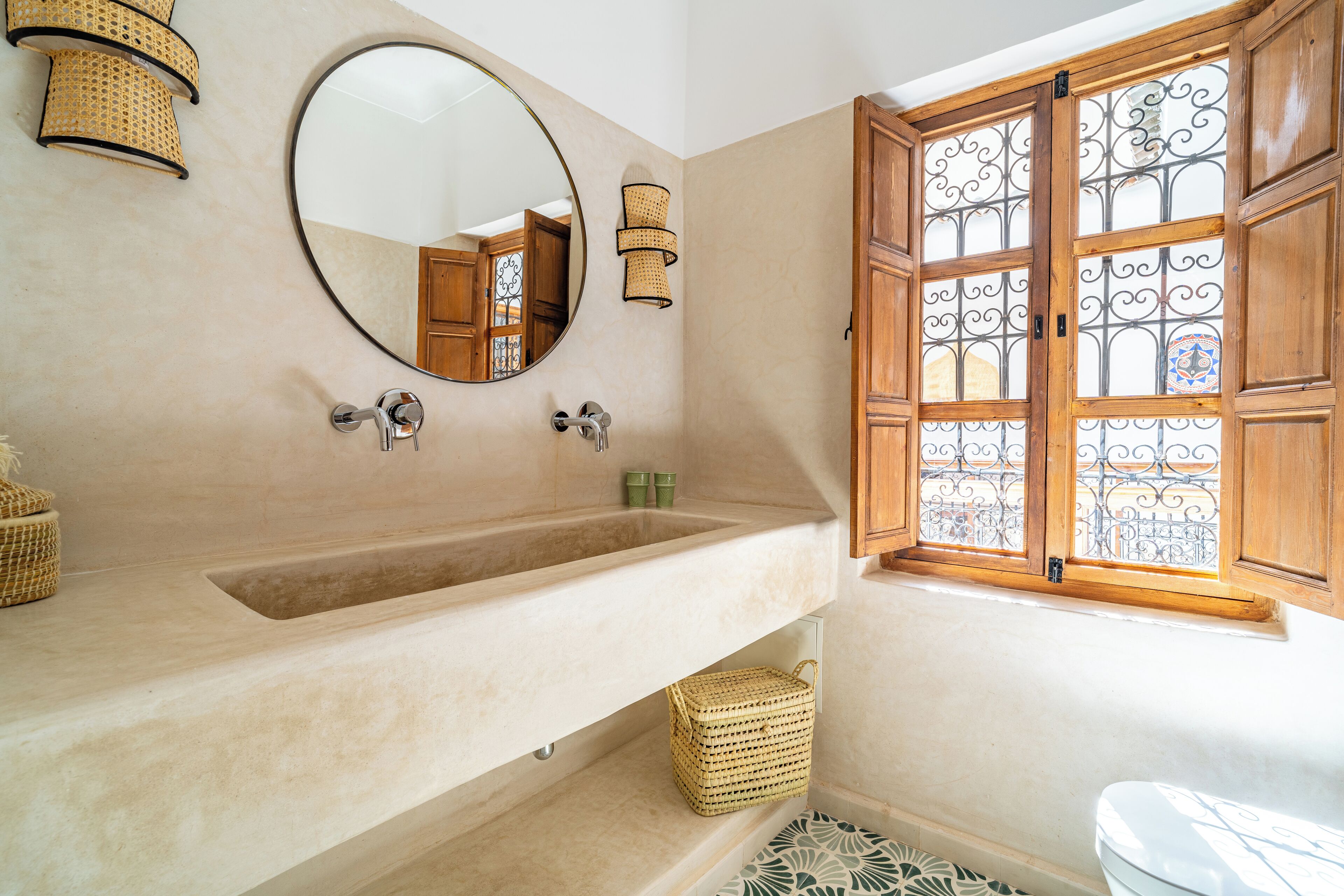 A bathroom with a large sink, a mirror, wicker baskets, and a window with decorative iron bars.