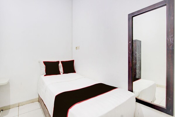 A bedroom with a bed, two pillows, a bedside table, and a large mirror. - Hotel O Guest House Sakinah (Purwokerto)