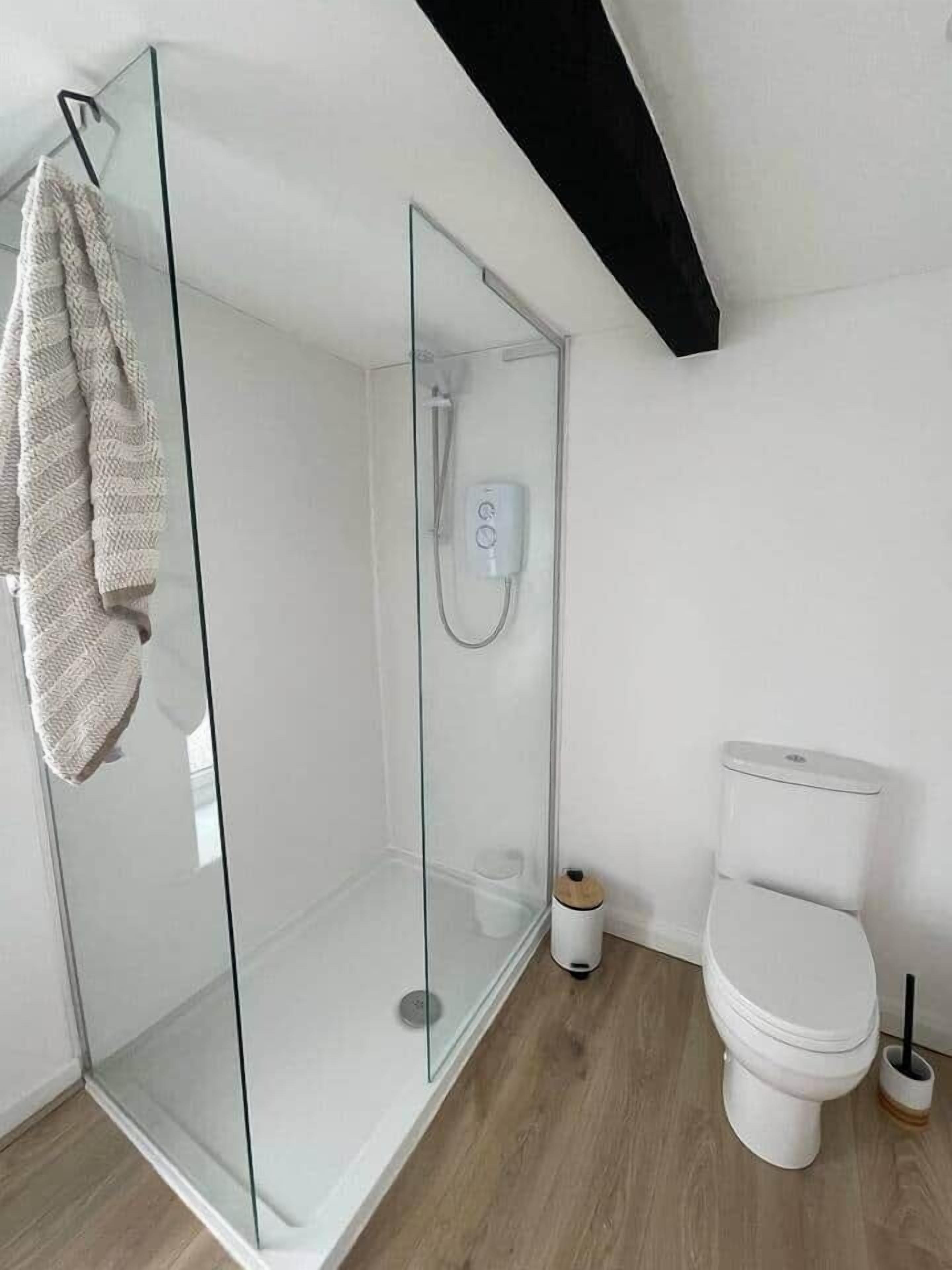Une salle de bain moderne avec une douche à parois de verre, des toilettes blanches et un plancher en bois.