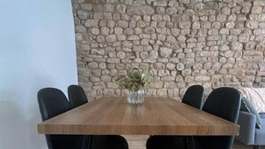 Uma mesa de jantar com seis cadeiras pretas, um vaso com plantas verdes e uma parede de pedra ao fundo.
