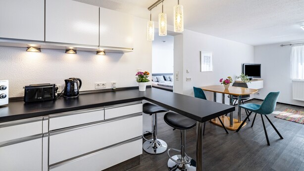 A modern kitchen with a bar area, a dining table with chairs, and a TV in the background. - The Old Tailoring Shop (Balingen)
