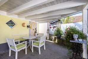 A patio area with a white table and chairs, a small window, and a decorative wall with a moon and heart-shaped ornaments.