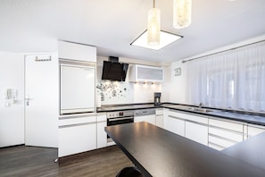 A modern kitchen with white cabinetry, a black countertop, a built-in oven, and a window with sheer curtains.