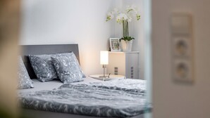 A neatly made bed with patterned pillows, a bedside table with a lamp, and a potted orchid on a shelf. - The Old Tailoring Shop (Balingen)