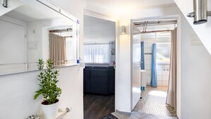 A narrow hallway with a potted plant, a small shelf, and a door leading to a bathroom with a shower curtain. - The Old Tailoring Shop (Balingen)