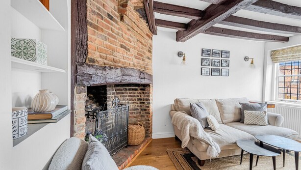 A cozy living room with a brick fireplace, a sofa, a coffee table, and a bookshelf. - Dolphin Cottage, Oxfordshire, England (Oxfordshire)