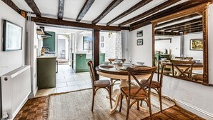 A dining area with a round table, wooden chairs, and a rustic ceiling. - Dolphin Cottage, Oxfordshire, England (Oxfordshire)