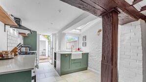 A modern kitchen with a large island, white brick walls, and a rustic wooden beam. - Dolphin Cottage, Oxfordshire, England (Oxfordshire)