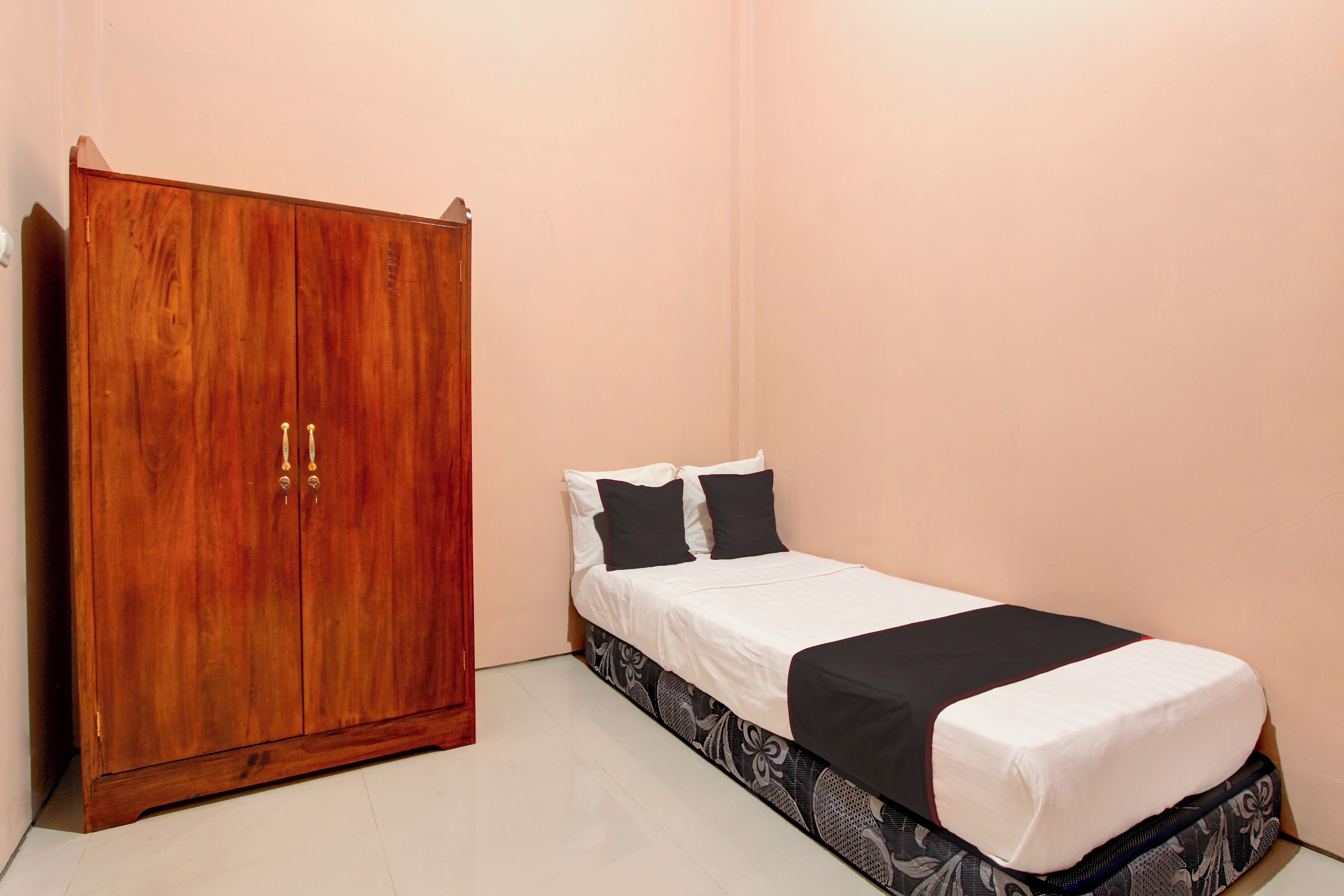 A bedroom with a wooden wardrobe, a bed with black and white bedding, and a patterned bed skirt.