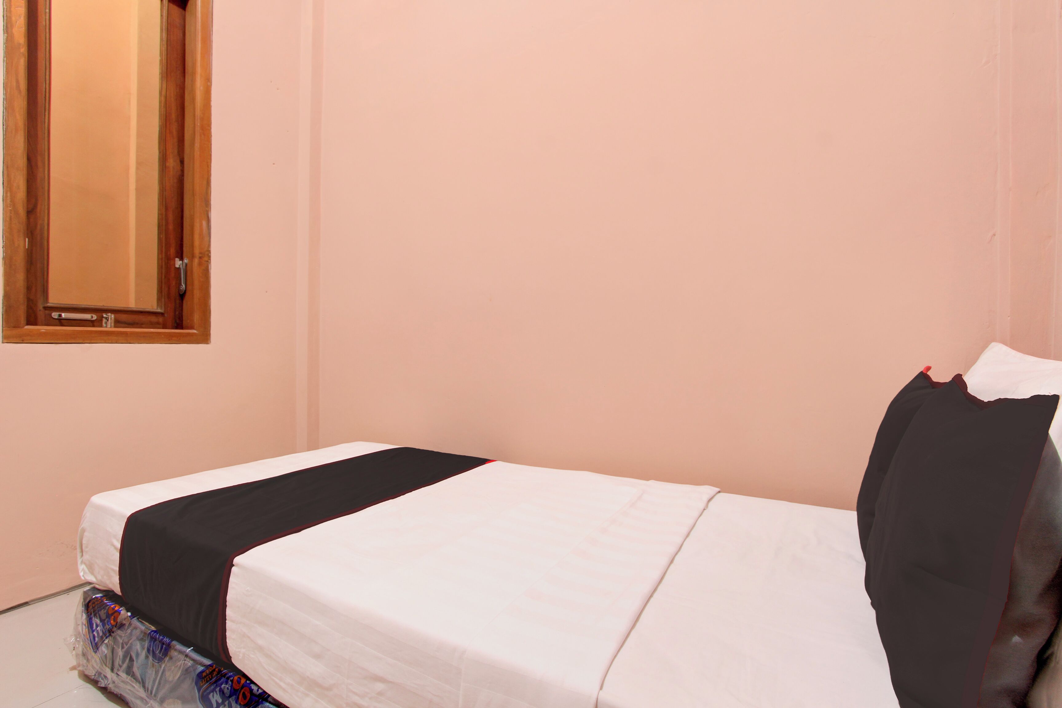 A single bed with a white mattress and black bedding, a wooden door, and a wall-mounted mirror.