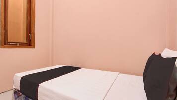 A single bed with a white mattress and black bedding, a wooden door, and a wall-mounted mirror.