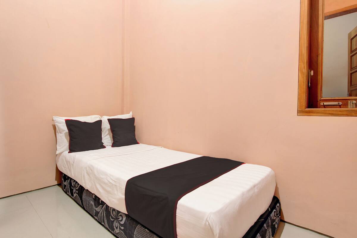 Una cama individual con ropa de cama blanca y negra, una falda estampada y un cabecero de madera.
