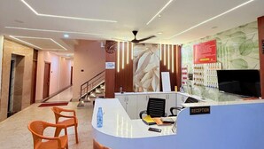 A reception area with a curved reception desk, two orange chairs, a clock, and a wall with a calendar.