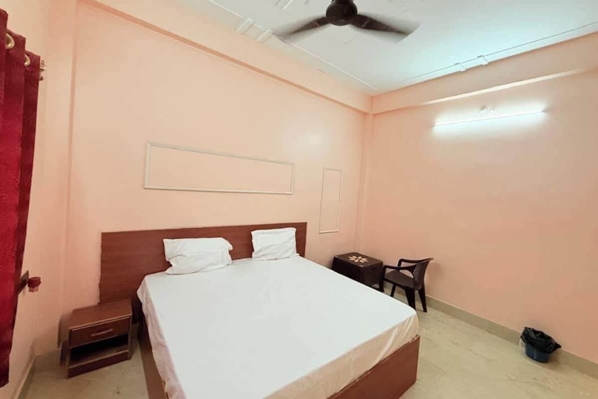 Quarto com cama, mesa de cabeceira, cadeira, mesinha e ventoinha no teto.
