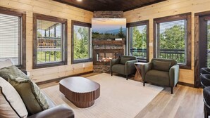 A cozy living room with a fireplace, large windows, and wooden walls. - New Modern 4BR Mtn Home w/ Indoor Pool, Rooftop Patio, Game Room, & Hot Tub (Pigeon Forge)