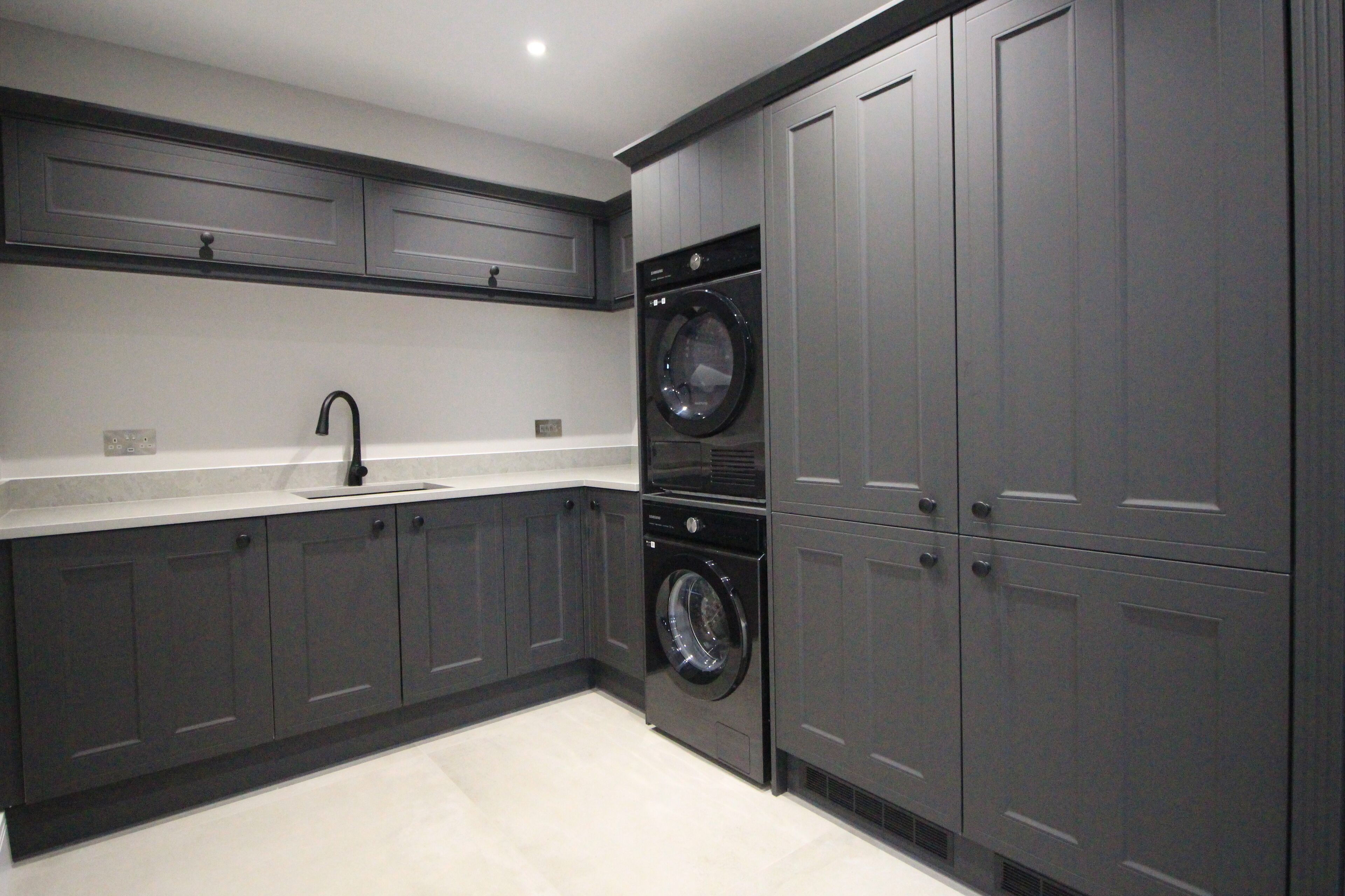 A modern kitchen with grey cabinetry, a double sink, and a built-in washer and dryer.