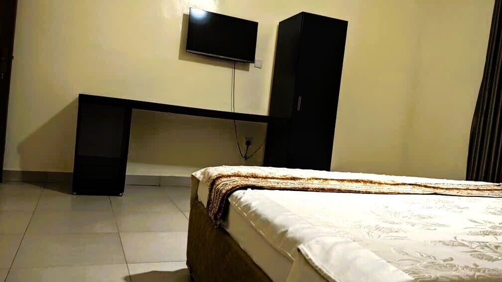 Un dormitorio con una cama, un escritorio y un televisor fijado en la pared.