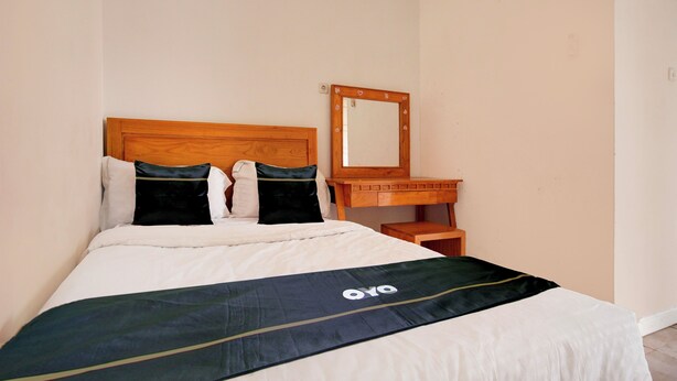Un lit bien fait, recouvert d’une couvre-lit noire et verte, avec une tête de lit en bois et un miroir placé au-dessus d’une table de chevet en bois.