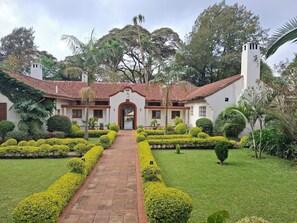 A building with a central entrance, surrounded by well-manicured gardens and trees. - ACK St.Julians Centre (Limuru)
