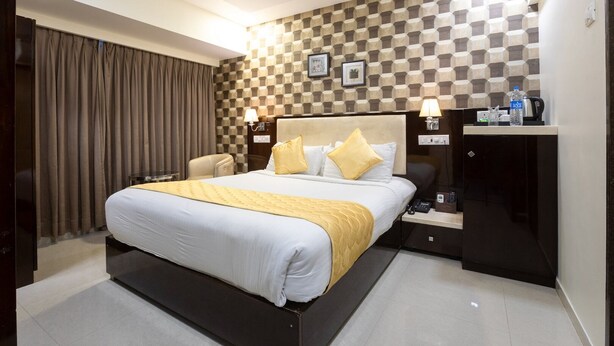 A hotel room with a large bed, a desk, a chair, a wardrobe, and a ceiling fan. - Hotel Laaiba Residency (Mumbai)