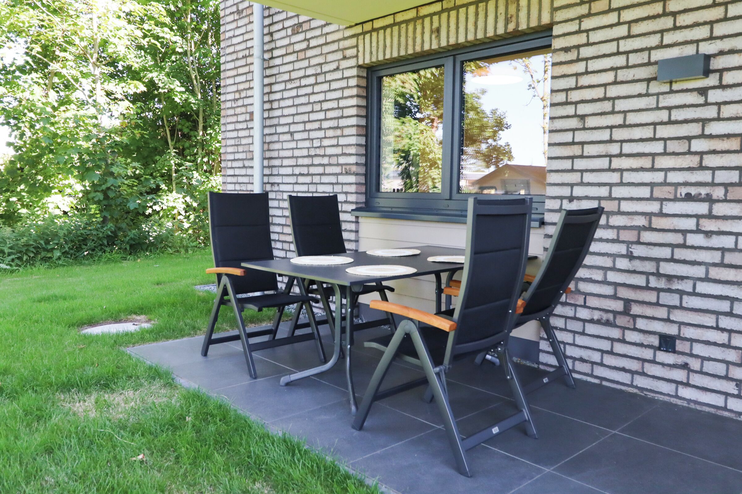 A patio with a brick wall, a table with chairs, and a window overlooking greenery.