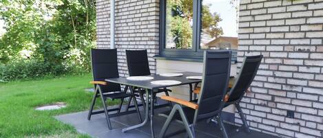 A patio with a brick wall, a table with chairs, and a window overlooking greenery.