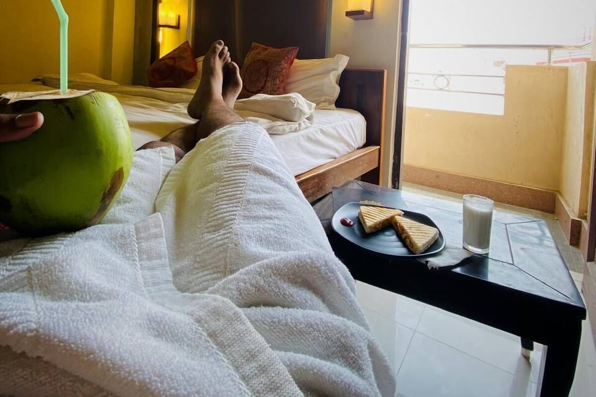A hotel room with a bed, a bedside table with a glass of milk, a plate with sandwiches, and a green coconut with a straw.