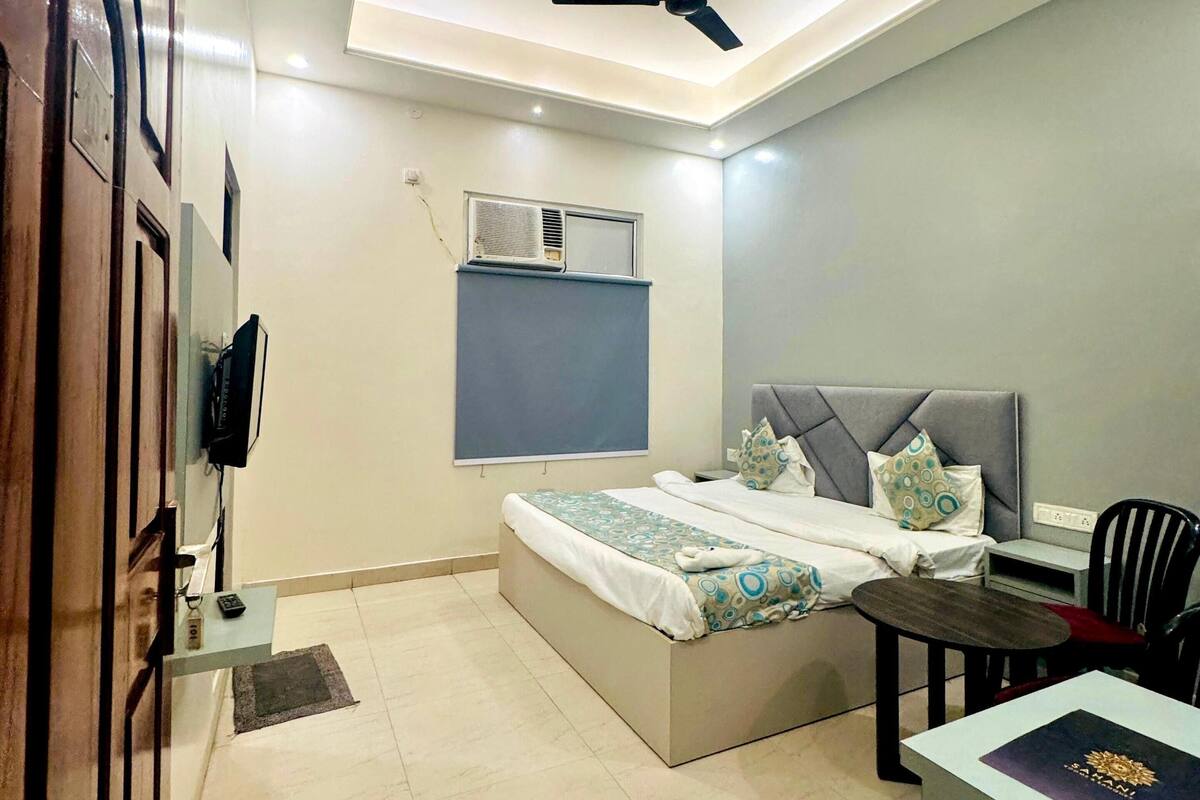 A modern bedroom with a bed, a desk, a chair, a ceiling fan, and an air conditioning unit.