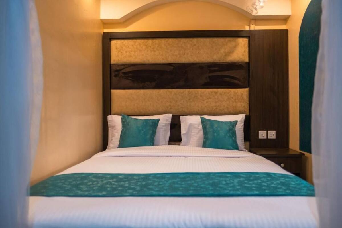A neatly made bed with white and teal bedding, a dark headboard, and a small bedside table with a lamp.