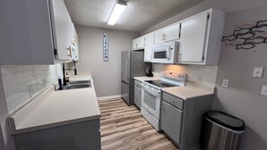 Una cocina compacta con armarios blancos, un refrigerador de acero inoxidable, un microondas y un horno.
