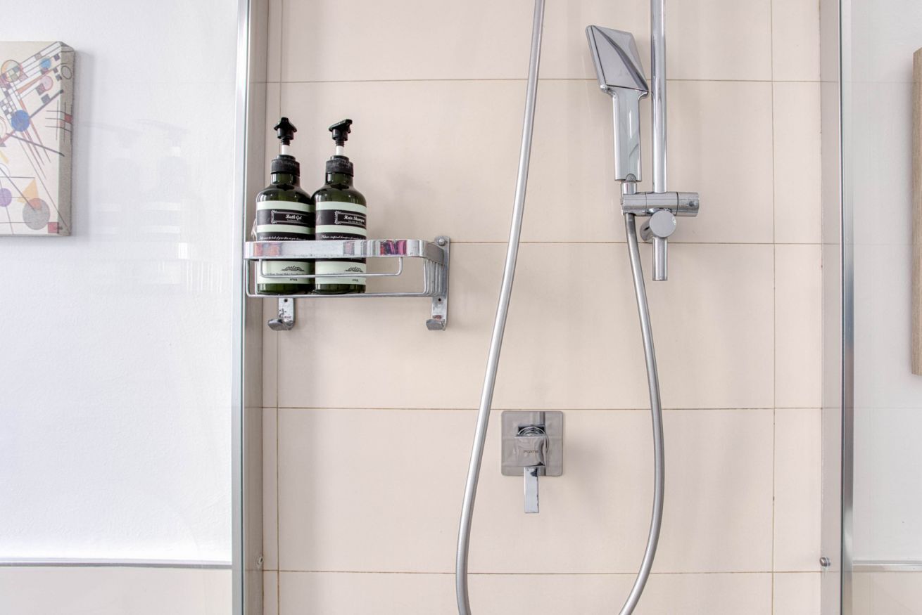 A shower area with a handheld showerhead, a wall-mounted faucet, and a soap dispenser.
