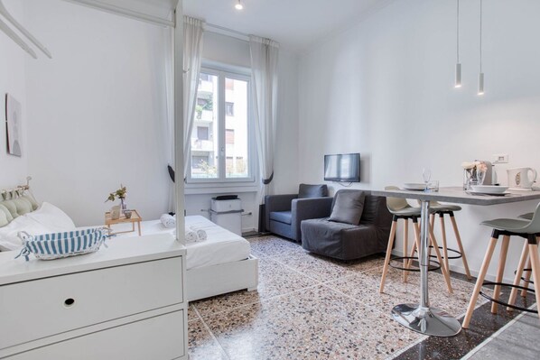 Une chambre d’hôtel moderne comprenant un lit, un canapé, une table à manger avec des chaises, une télévision et une fenêtre avec des rideaux.