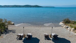 Ein Strand mit zwei Sonnenschirmen und Liegestühlen vor einem ruhigen Meer.