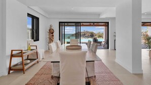 Un espace repas moderne, doté d’une grande table, de chaises et offrant une vue sur l’océan.