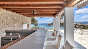 Une cuisine extérieure moderne, avec un mur en pierre en arrière-plan, un évier intégré et une vue sur la mer.