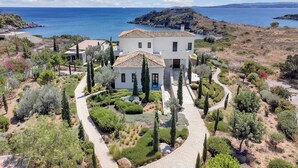 Une maison à deux étages, dotée d’un toit en tuiles, entourée d’un jardin aménagé avec des allées et divers arbustes.
