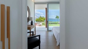 A bedroom with a large sliding glass door leading to a balcony with a view of the sea.
