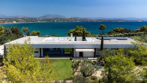 A modern house with a flat roof, solar panels, and a view of the sea and mountains.