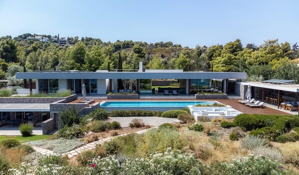 Une maison moderne à deux étages, dotée d’une piscine, d’un espace extérieur aménagé et offrant une vue sur la verdure environnante.