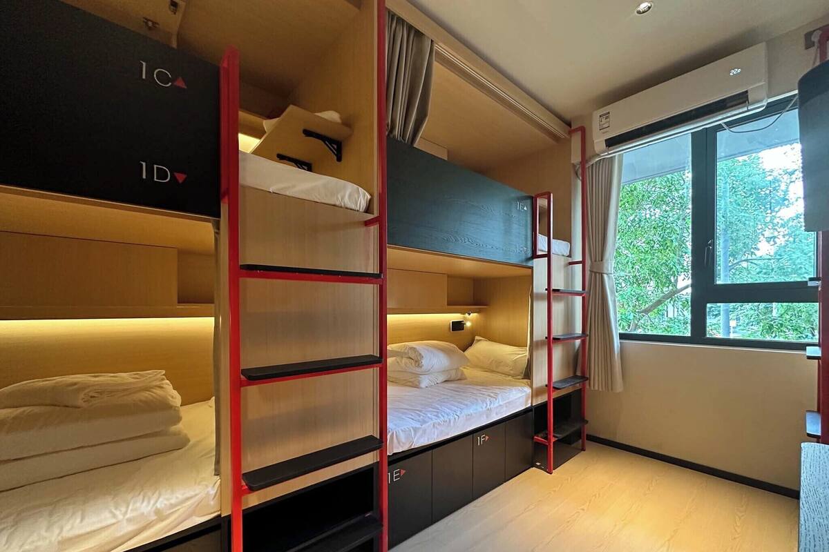 A bunk bed room with a ladder, a window with a view of trees, and an air conditioning unit.