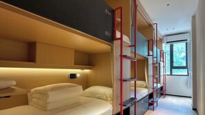 Une chambre d’hôtel moderne avec des lits superposés, un plancher en bois et une fenêtre laissant entrer la lumière naturelle.
