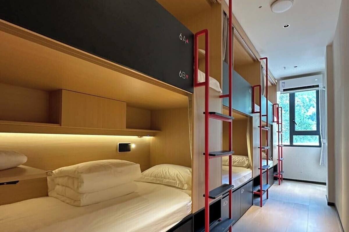 A modern hotel room with bunk beds, a wooden floor, and a window providing natural light.