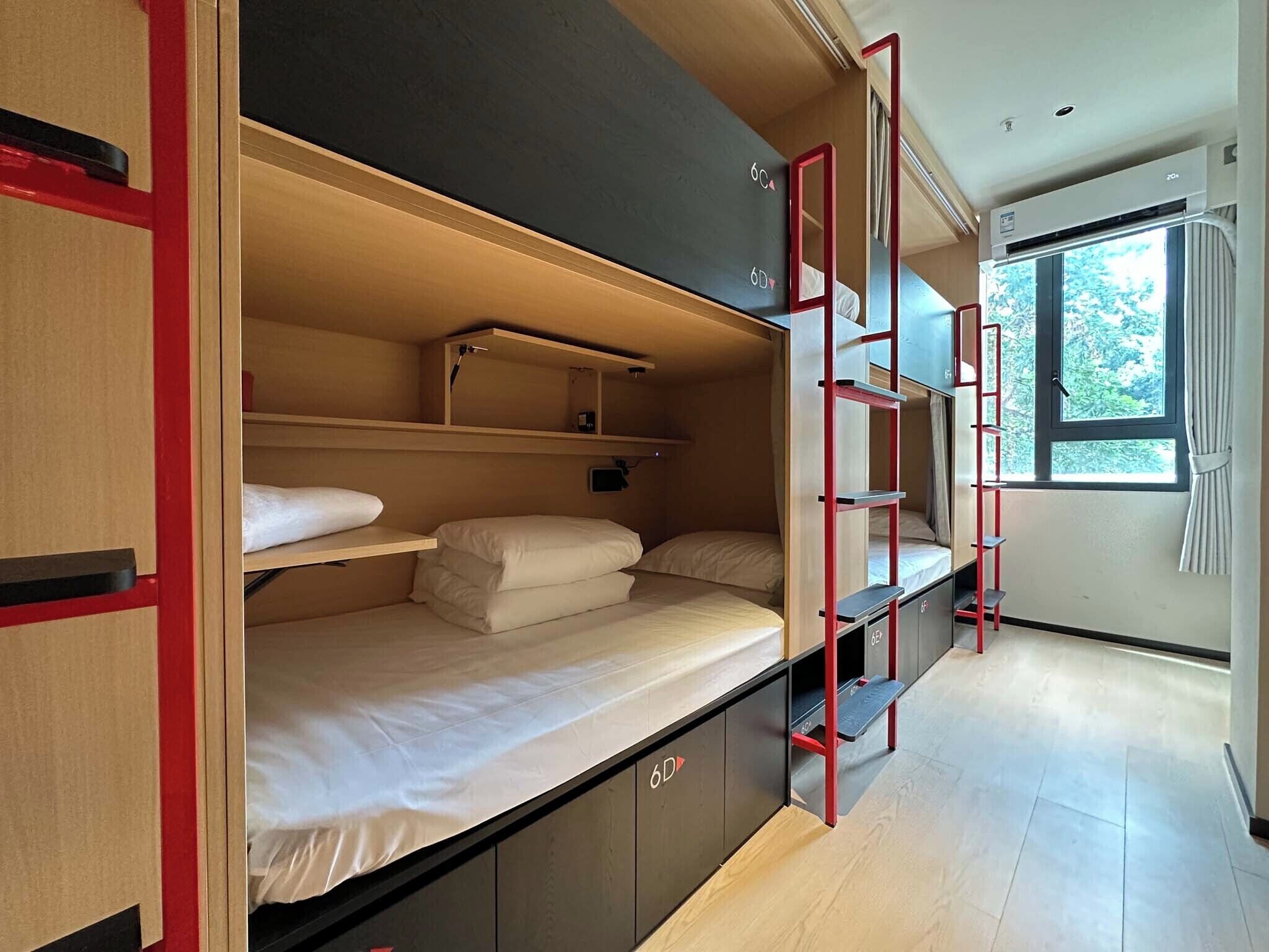 A compact, modern room with bunk beds, a ladder, and a window with a view of greenery.