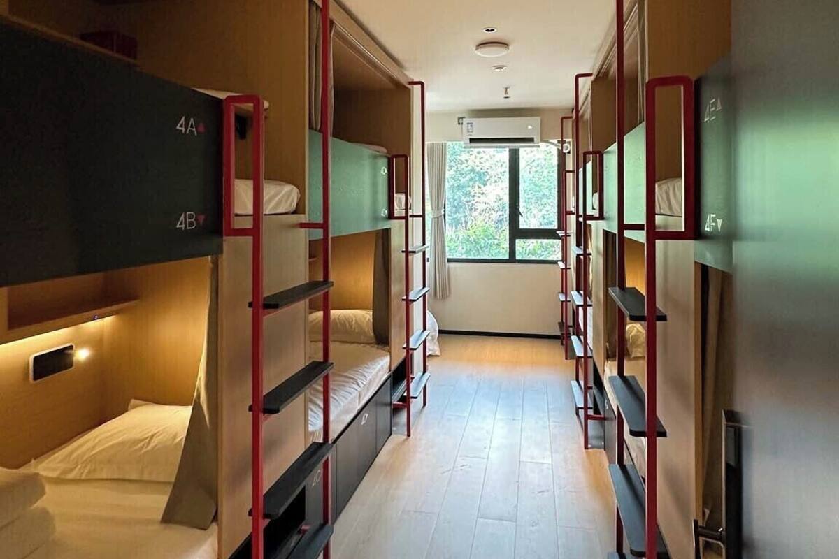 A corridor with bunk beds, wooden flooring, and a window at the end.