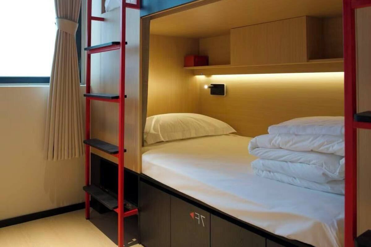 A bunk bed room with a ladder, a small shelf, and a window with curtains.
