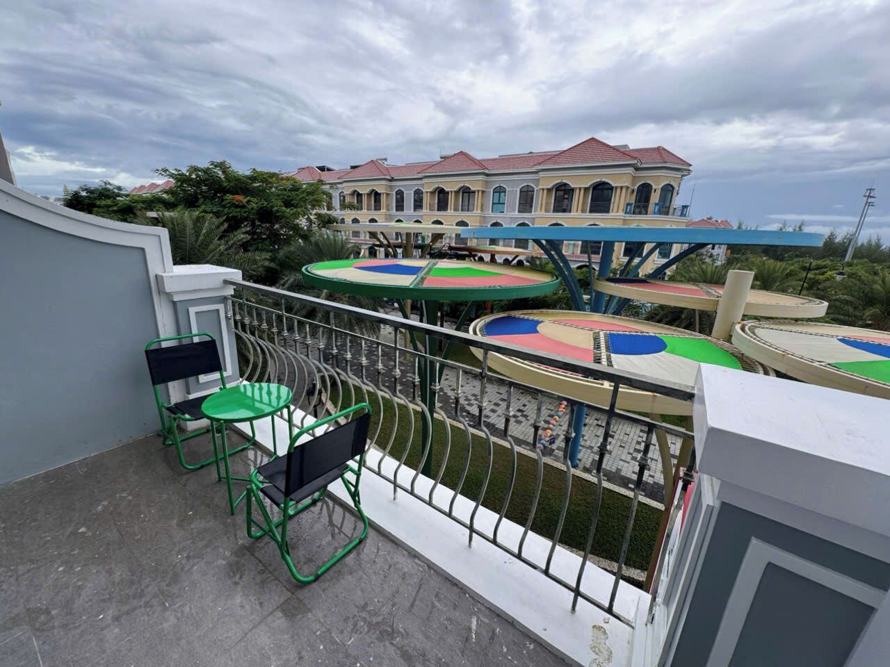 Un balcon avec des chaises vertes et une vue sur une aire de jeux aux couleurs vives.