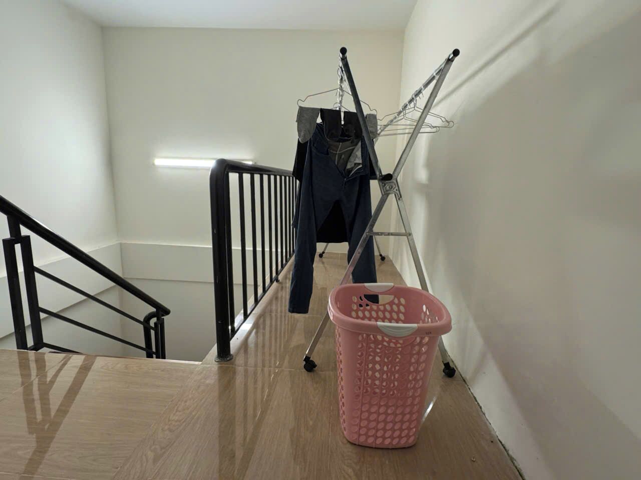 A staircase with a metal handrail, a pink laundry basket, and a clothes drying rack with dark clothing.